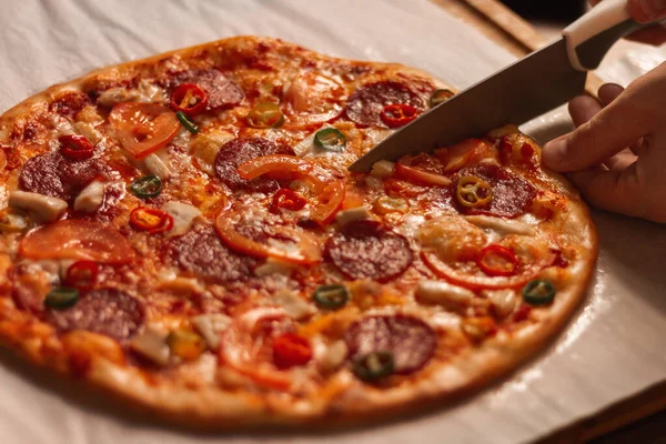 Pizzayı bıçakla kesmek. Acı biberli pizza, biberli ve domatesli..