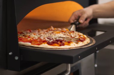 Pizzayı fırına Cook koydu. Mantarlı, domatesli, salamlı, sosisli, etli ve peynirli çeşitli pizza..
