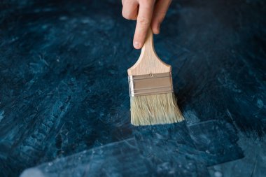 Mavi boyalı yüzeyin vernik kaplaması. Bir adamın eli mavi boyalı bir yüzeye vernik uygulamak için boya fırçası kullanır..