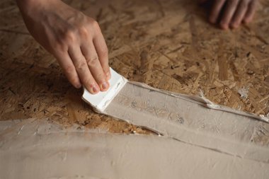 El, macuna spatula sürer. Oyun macunu OSB plakasına uygulanıyor