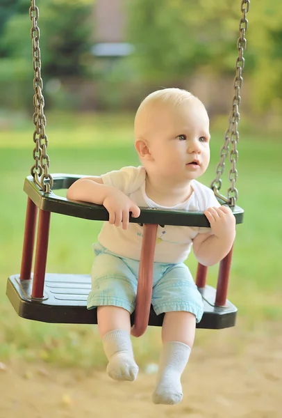 Buon bambino che si diverte su un giro swing in un parco giochi Foto Stock