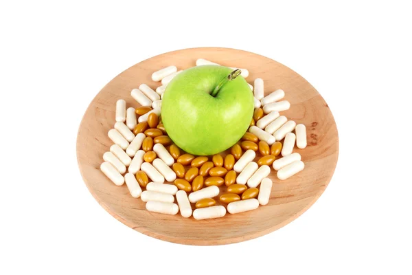 Pillole su piatto di legno e una mela isolata su bianco — Foto Stock