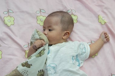 Yatakta yatarken gülümseyen Asyalı Çinli bebek. Mutlu yeni doğan çocuk yatakta dinleniyor.