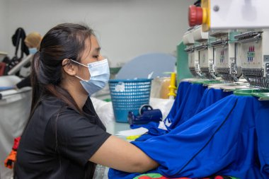 Kota Kinabalu, Sabah, Malezya-15 Aralık 2020: Koruyucu yüz maskeli ve nakış tekstil üreticilerinde çalışırken sosyal mesafeyi koruyan kadın işçiler