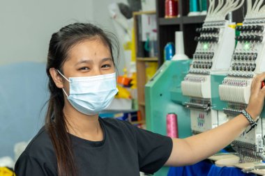 Kota Kinabalu, Sabah, Malezya-15 Aralık 2020: Koruyucu yüz maskeli ve nakış tekstil üreticilerinde çalışırken sosyal mesafeyi koruyan kadın işçiler