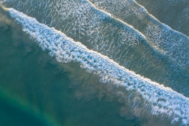 Okyanus dalgaları ve suyun kumlu sahile yukarıdan çarptığı güzel bir sahil görüntüsü.