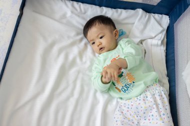 Mutlu yerel yaşam tarzının portresi. Asyalı Çinli bebek tek başına oynuyor ve bebek yatağında dolaşıyor.