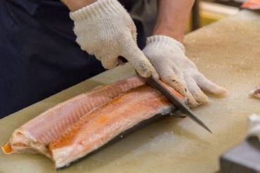 Suşi şefi taze somon balığı dilimliyor, suşi şefi beyaz koruluk giymiş taze somon balığı dilimliyor.