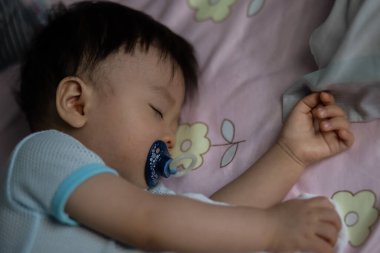 Küçük Asya 'lı çocuk emzik emerek yatakta uyuyor.