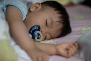 Küçük Asya 'lı çocuk emzik emerek yatakta uyuyor.