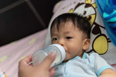 Asyalı Çinli çocuk süt şişesini tek başına tutuyor..