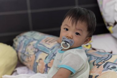 Yatağında emzik emziren tatlı bir erkek bebeğin portresi.