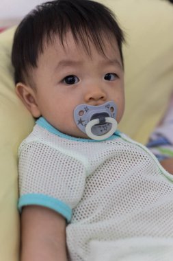 Yatağında emzik emziren tatlı bir erkek bebeğin portresi.