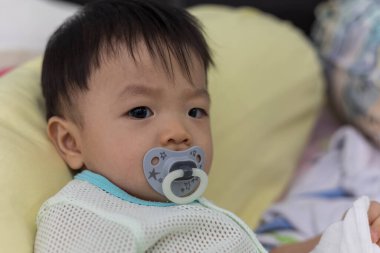 Yatağında emzik emziren tatlı bir erkek bebeğin portresi.