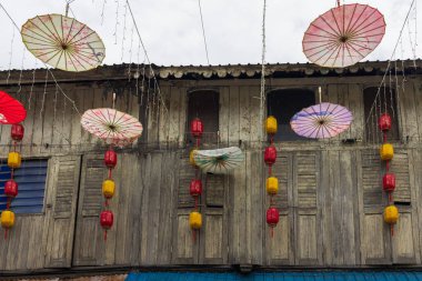 Kuching, Sarawak, Malezya - 14 Nisan 2025: Kırmızı ve sarı kağıt fenerler ve eskimiş ahşap cepheden sarkan renkli şemsiyeler.