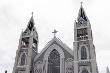 Kilise binası, karmaşık mimari, saat kuleleri ve bulutlu bir gökyüzüne karşı belirgin bir haç.