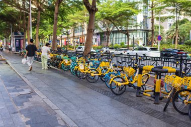 Zhuhai, Guangdong, Çin - 15 Mayıs 2025 kaldırımda yürüyen yayalar büyük bir Çin şehrinde parkedilmiş renkli bisikletleri paylaşıyorlar.