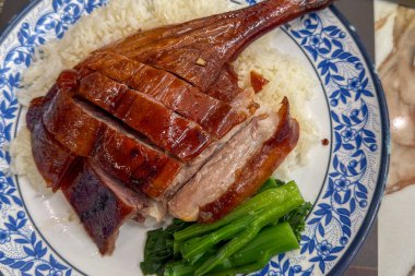 Dilimlenmiş ördek bacağı, pirinçle servis edilmiş yeşil sebzeler ve dekoratif tabakla lezzetli ve görsel olarak çekici bir mutfak deneyimi sunuyor.