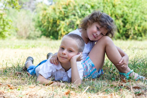 Kleine jongen en het meisje liggen samen op een gras — Stockfoto