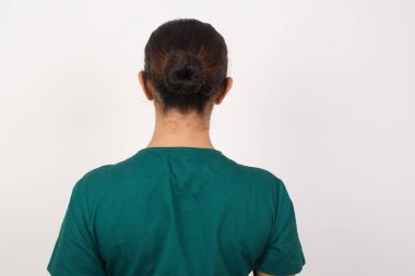 Beyaz duvarın karşısında duran genç beyaz bir kadının arka görünüşü. Stüdyo Çekimi.