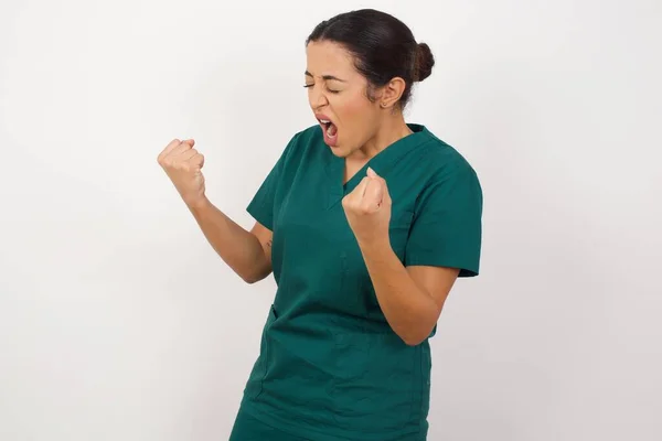 美しい若い看護師は非常に満足し 腕を上げて勝者のジェスチャーを行う興奮し 笑顔と成功のために叫んでいます お祝いのコンセプト — ストック写真