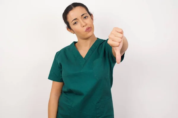 ウォールに対して真剣な表情で親指を出す美しい若い看護師 — ストック写真