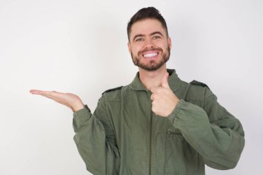 Model avuç içini gösteriyor ve baş parmaklarıyla iyi bir hareket yapıyor, mutlu ve neşeli gülümsüyor..