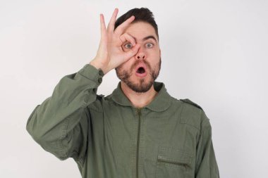 İyi davranan genç bir Arap, şaşırmış bir yüz ve parmaklarından bakan bir gözle şaşırmış bir şekilde hareket ediyor. İnançsız ifade.