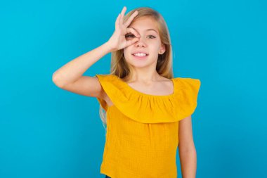 Küçük kız el hareketleriyle gülümsüyor, gözleriyle mutlu yüzüyle parmaklarının arasından bakıyor..