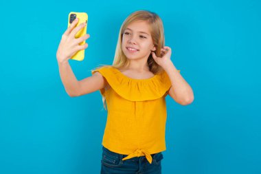 Küçük kız gülümsüyor ve selfie çekiyor. Sosyal medyada paylaşmaya hazır..