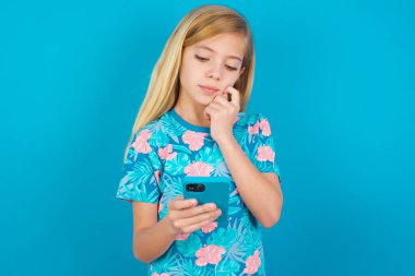 Düşünceli, mutlu, beyaz bir çocuk elinde telefon tutuyor.