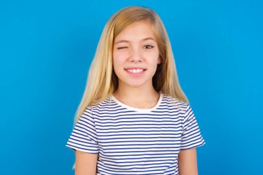 Cimri beyaz çocuk mutlu bir şekilde gülümsüyor, kameraya şakacı bir şekilde göz kırpıyor, seninle flört ediyor..