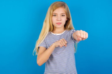 Mavi duvara karşı çizgili gömlek giyen beyaz bir kız. Yumruk yumruğa dövüş, agresif ve öfkeli saldırı, tehdit ve şiddet