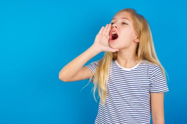 Caucasian girl wearing striped shirt against blue wall shouting and screaming loud to side with hand on mouth. Communication concept. clipart