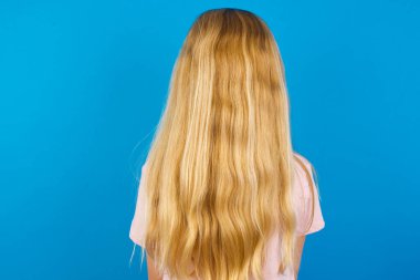 Mavi duvara karşı pembe gömlek giyen beyaz bir kızın arka görüntüsü. Stüdyo Çekimi.