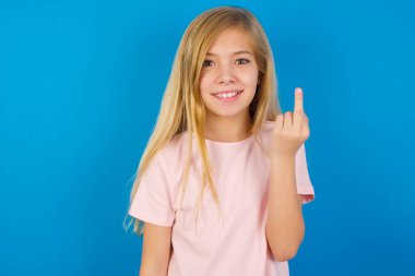 Mavi duvara karşı pembe tişört giyen beyaz bir kız orta parmak kötü işaretinin rahatsız etmediğini gösteriyor. Kışkırtma ve kaba tavır.