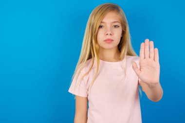 Mavi duvara karşı pembe tişört giyen beyaz kız dur işareti gösteriyor. Avuç içini kameraya sert bir ifadeyle yaklaştırıyor.