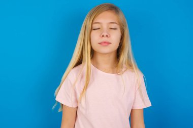 Mavi duvara karşı pembe tişört giyen beyaz kız hoş görünümlü, sevimli, çekici, sevimli, sevimli, sevimli, tatlı, huzurlu, kapalı gözler.