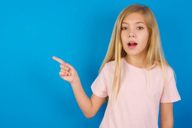 Mavi duvara karşı pembe tişört giyen beyaz bir kızın şoktan çenesini indirmesi, boş alandaki inanılmaz reklam noktalarını gösteriyor. Bu da büyük bir alışveriş satışını gösteriyor. Reklam.