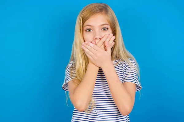 青い壁に縞模様のシャツを着た白人の子供は間違いのために手で口をカバーショックを受けた 秘密概念 — ストック写真