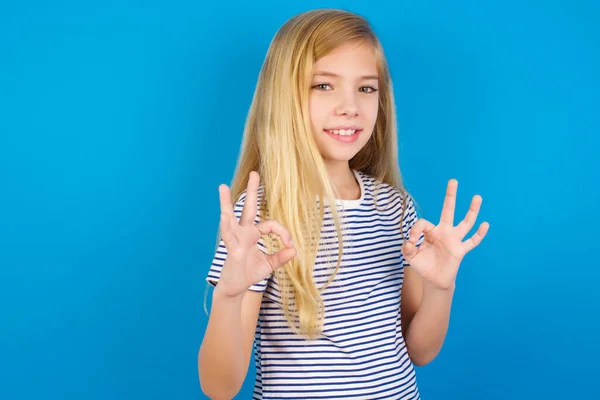 青い壁に縞模様のシャツを着た白人の子供は 両手を指でOkサインで示しています コンセプトの承認または推奨 — ストック写真