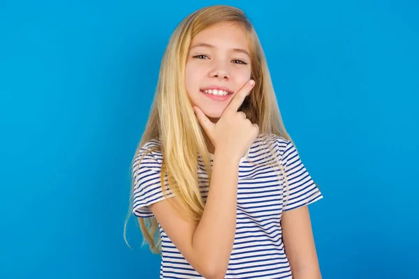 青い壁に縞模様のシャツを着た白人の少女は カメラを見て自信を持って交差腕と手をあごに提起笑みを浮かべて 肯定的な考え — ストック写真
