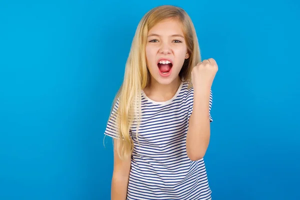ブルーの壁に縞模様のシャツを着た白人の女の子は怒りながら叫びながら 怒りと怒りの拳不満と怒りを上げ怒っています 激怒と積極的な概念 — ストック写真