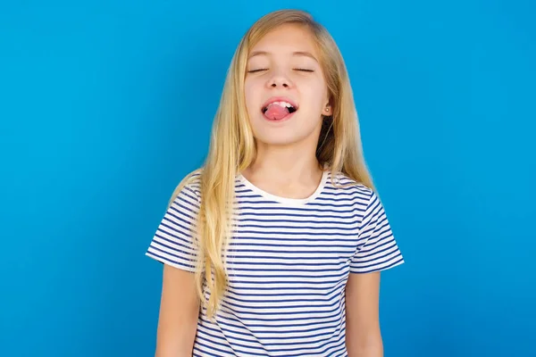青い壁にストライプのシャツを着た白人の女の子が面白い表情で幸せ舌を突き出しています 感情概念 — ストック写真