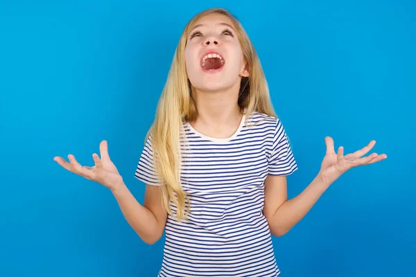 白种人女孩穿着条纹衬衫 靠着蓝色的墙疯狂地喊着 带着咄咄逼人的表情和胳膊大喊着 沮丧的概念 — 图库照片
