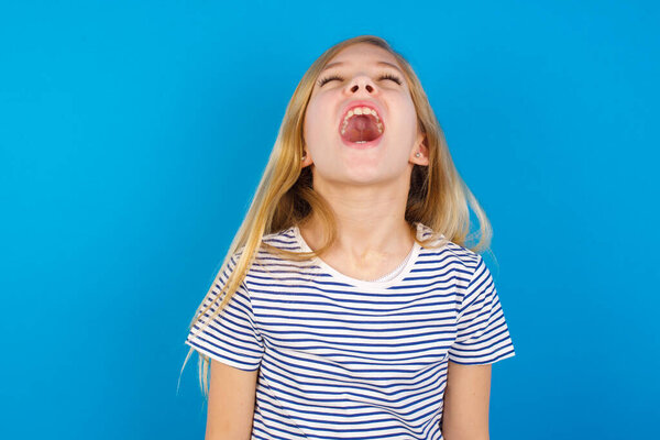 Caucasian girl wearing striped shirt against blue wall angry and mad screaming frustrated and furious, shouting with anger. Rage and aggressive concept.