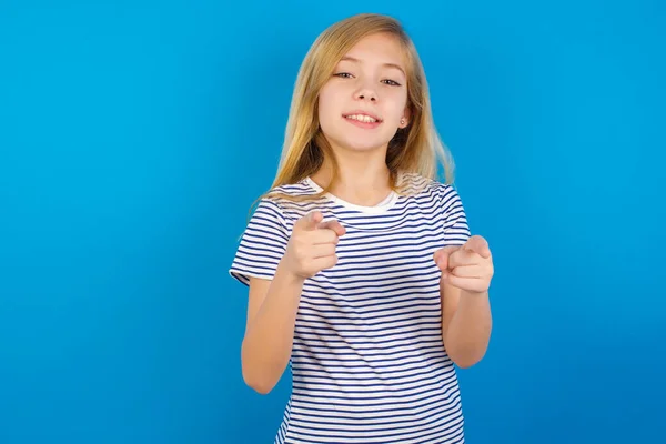 青い壁に縞模様のシャツを着た白人の少女が 楽しそうにカメラを指差している 良いエネルギーと振動 — ストック写真