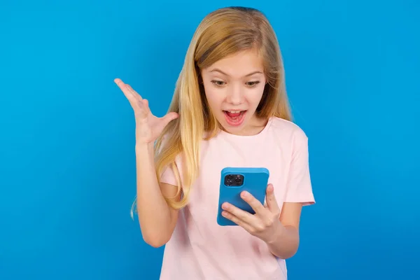 Blank Meisje Draagt Roze Shirt Tegen Blauwe Muur Handen Cel — Stockfoto