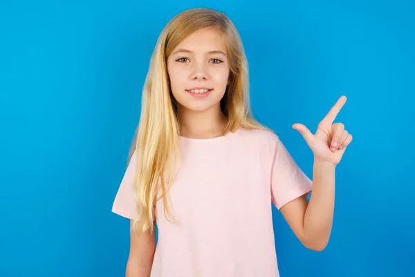 Biały Dzieciak Dziewczyna Noszenie Różowy Koszula Przeciw Niebieski Ściana Wskazując — Zdjęcie stockowe