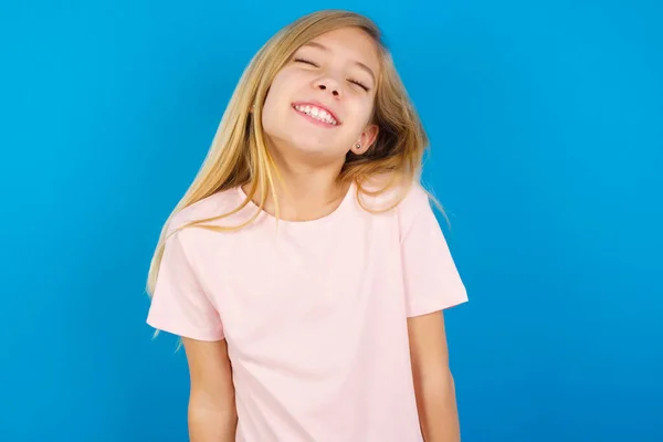 積極的な白人の子供の女の子身に着けていますピンクシャツに対して青壁とともに喜びました式閉じます目と笑いショー白完璧な歯 — ストック写真